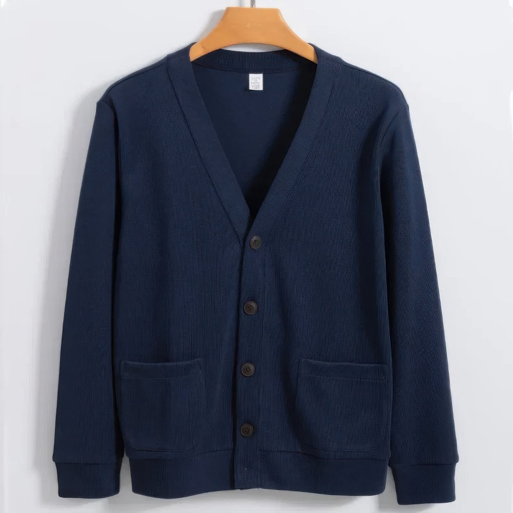 Cardigan blu scuro in cotone, con scollo a V, tre bottoni e due tasche frontali, appeso su gruccia di legno. Maglione elegante e casual.