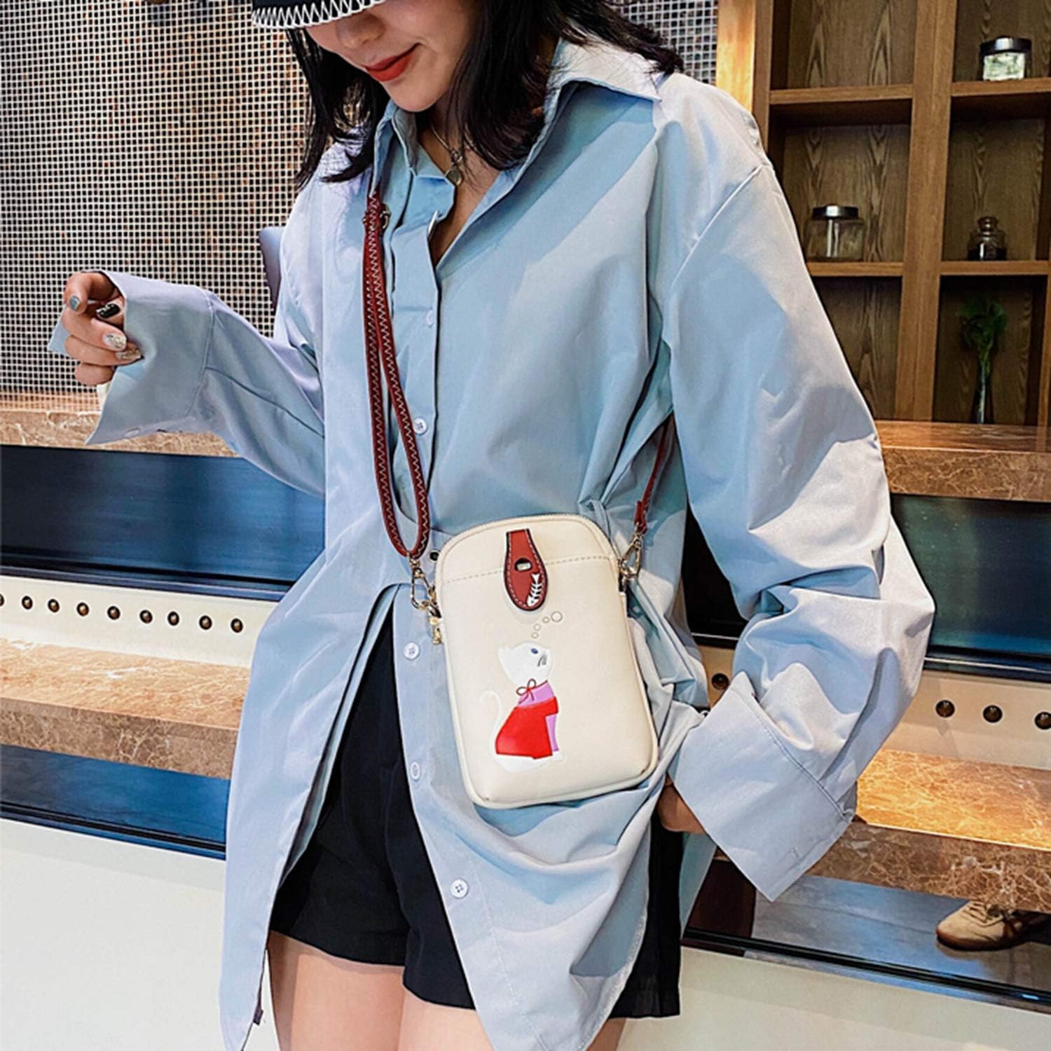 Donna con camicia azzurra oversize, pantaloncini neri e borsa a tracolla bianca con stampa. Stile casual chic, moda femminile contemporanea.