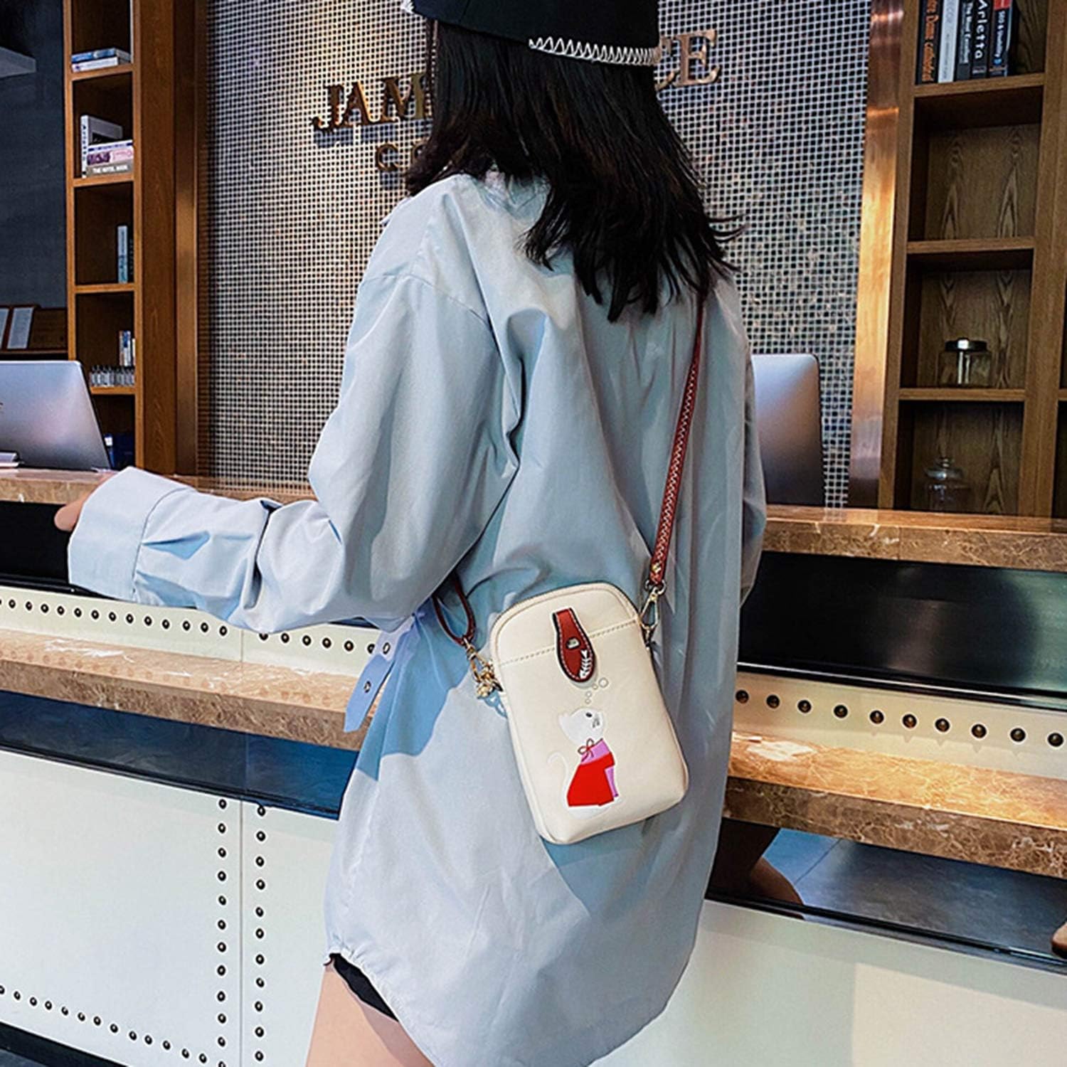 Donna con camicia azzurra e borsa a tracolla bianca con stampa rossa, in un ambiente moderno. Accessorio moda femminile, stile casual chic.