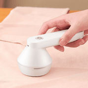 Rimuovi pelucchi elettrico bianco, portatile, in uso su tessuto rosa. Design ergonomico, ideale per abbigliamento e tessuti. Accessorio per la cura dei vestiti.