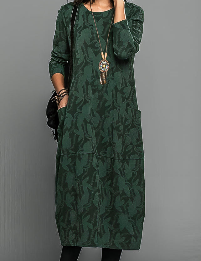 Abito lungo verde con motivo floreale, maniche lunghe, tasche frontali, collana pendente. Elegante e casual, perfetto per l'autunno.