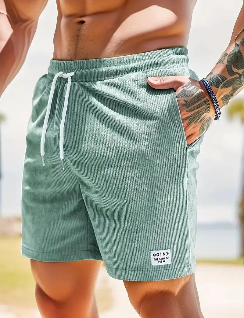 Uomo in costume da bagno verde menta a righe, con cordoncino bianco, in spiaggia. Moda estiva, abbigliamento mare, stile casual.