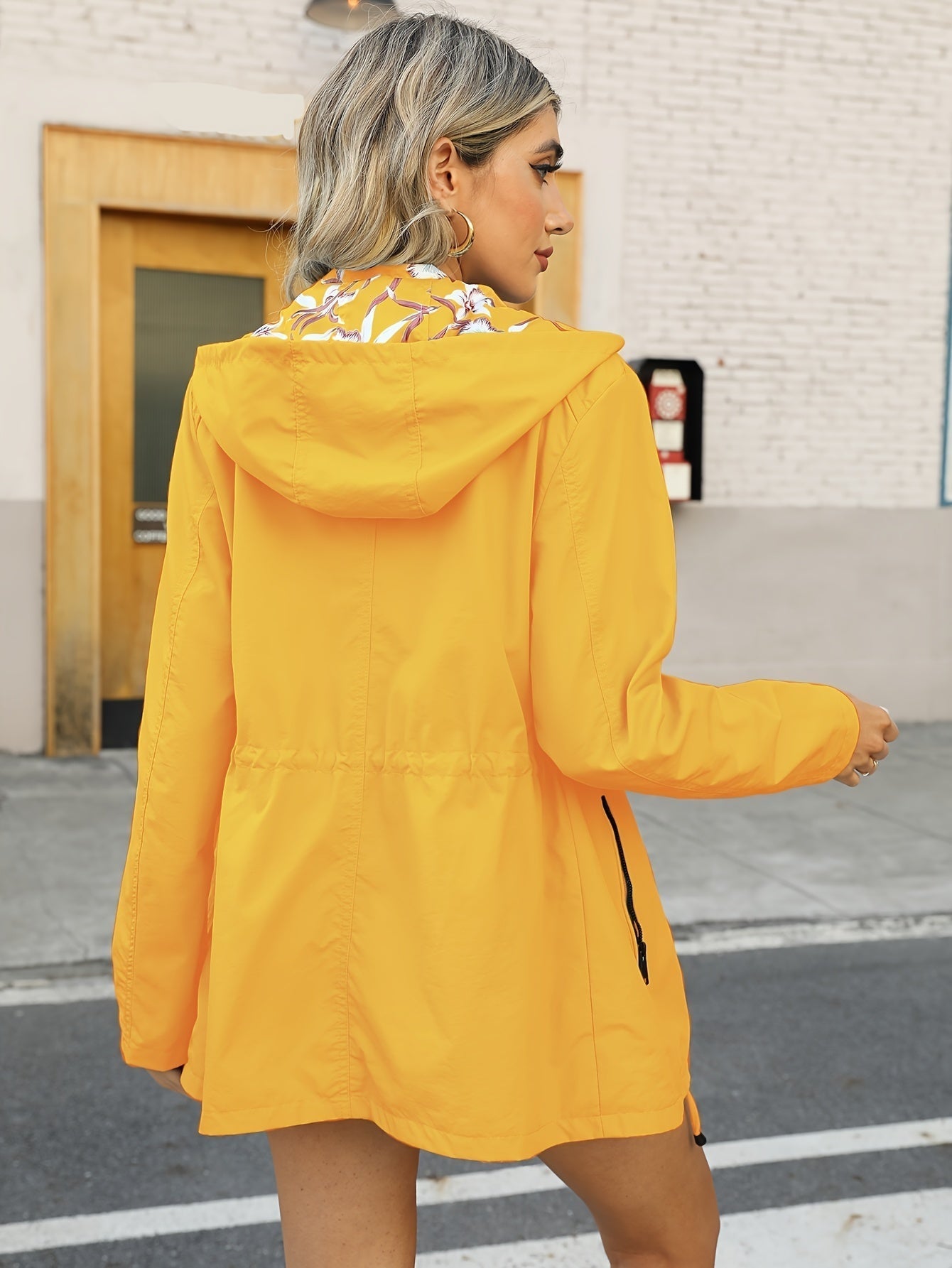 Donna con giacca impermeabile gialla, cappuccio e dettagli floreali, cammina in strada. Moda autunnale, abbigliamento casual, stile urbano.