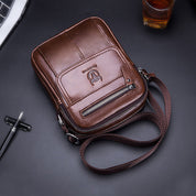 Borsa a tracolla in pelle marrone, design elegante con cerniera frontale e logo, ideale per uomo, accessorio moda, stile casual e pratico.