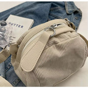Borsa a tracolla beige in tessuto a coste, con zip argentata, su sfondo di jeans e libro. Accessorio moda casual, elegante e versatile.