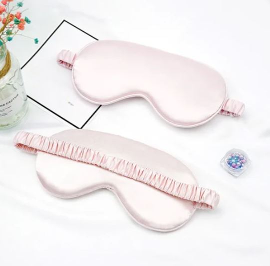 Mascherine per dormire in seta rosa su sfondo bianco, con elastico arricciato. Accessorio per il sonno, relax, benessere.