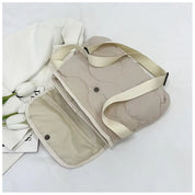 Borsa a tracolla beige trapuntata con chiusura a bottone, cinturino regolabile, su sfondo bianco con tulipani. Accessorio moda elegante e versatile.