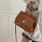 Borsa a tracolla marrone in pelle lucida, design elegante con chiusura dorata, indossata da una persona in abbigliamento casual. Accessorio moda donna.