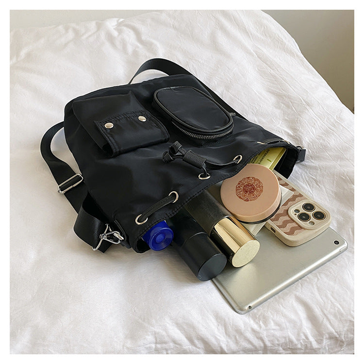 Zaino nero aperto su letto bianco, contenente cosmetici, smartphone e tablet. Accessori moda, tecnologia, bellezza, organizzazione viaggio.