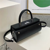 Borsa a mano nera elegante in pelle con tracolla regolabile, chiusura a scatto argentata, design moderno su sfondo minimalista.