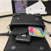 Borsa a tracolla nera aperta con smartphone colorato, power bank e custodia nera all'interno. Accessori moda, tecnologia portatile.