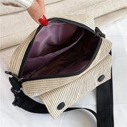 Borsa a tracolla in tessuto a coste beige con cerniera aperta, interno foderato in tessuto viola, tracolla regolabile nera, design casual e moderno.