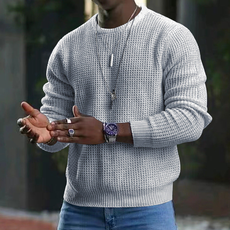 Maglione uomo grigio a maglia grossa, indossato con jeans blu. Accessori: orologio viola, collana e anelli. Stile casual autunnale.