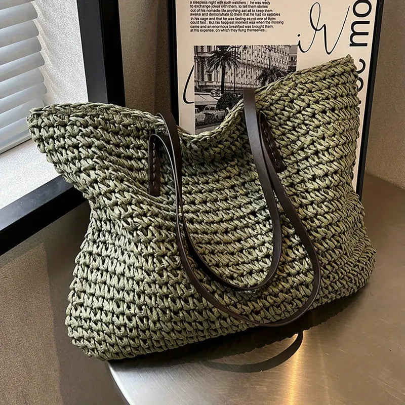 Borsa intrecciata verde oliva con manici in pelle marrone su tavolo, design elegante e moderno, perfetta per moda estiva e shopping.