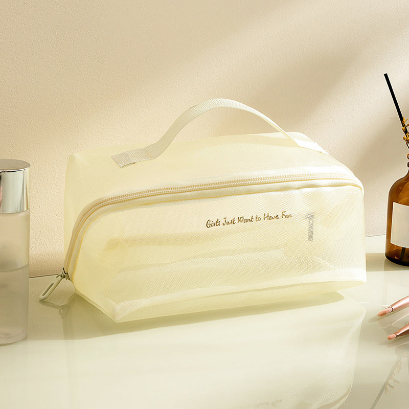 Borsa da toilette trasparente beige con cerniera, manico superiore e scritta "Girls Just Want to Have Fun", su tavolo con accessori da bagno.