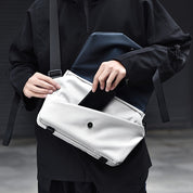 Borsa a tracolla moderna in tessuto bianco, con tasca frontale e chiusura a bottone, indossata da una persona in abbigliamento nero.
