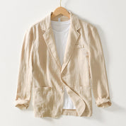 Giacca beige in lino su gruccia, con tasche frontali e maniche arrotolate, abbinata a t-shirt bianca. Elegante e casual, perfetta per l'estate.