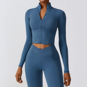 Donna in abbigliamento sportivo blu, top a maniche lunghe con zip e leggings a vita alta. Moda fitness, abbigliamento palestra donna.