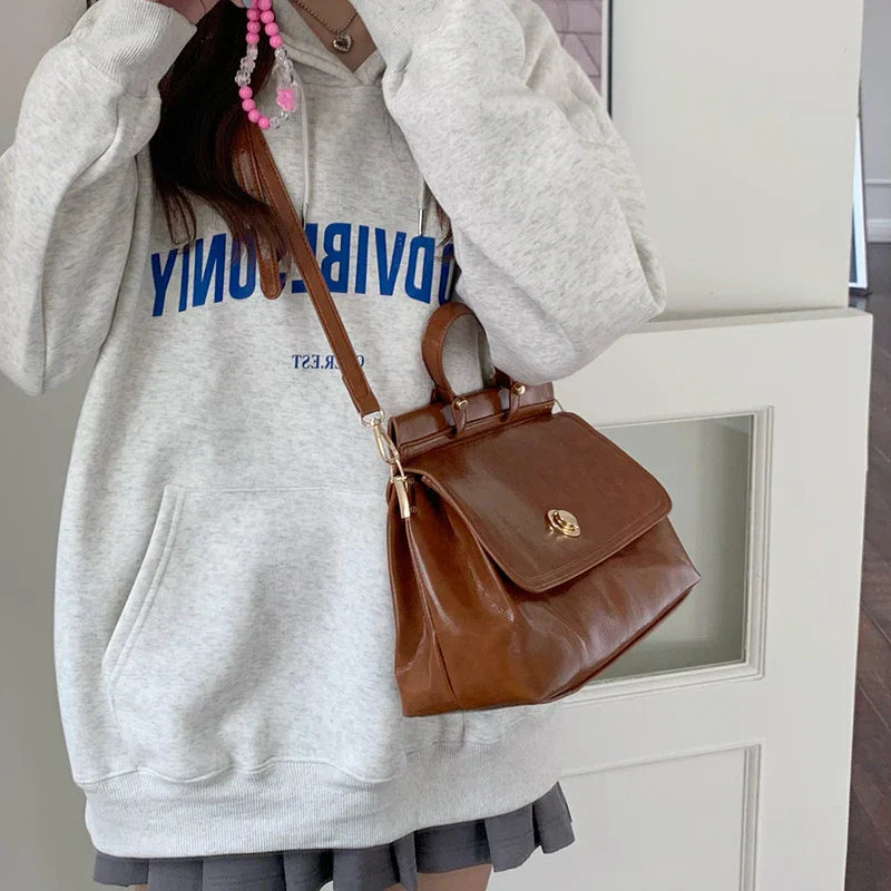Donna con felpa grigia e borsa a tracolla marrone in pelle, design elegante, moda casual, accessori femminili, stile urbano.