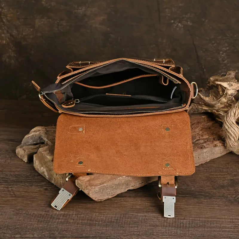 Borsa a tracolla in pelle marrone aperta, con scomparti interni visibili, su sfondo rustico in legno. Accessorio moda elegante e funzionale.