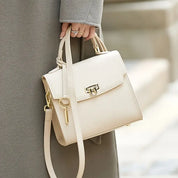Donna con cappotto grigio tiene borsa a tracolla beige elegante in pelle, chiusura dorata, design moderno. Accessorio moda femminile.