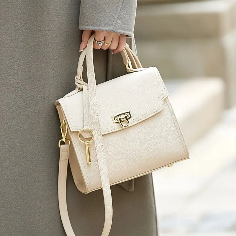 Donna con cappotto grigio tiene borsa a tracolla beige elegante in pelle, chiusura dorata, design moderno. Accessorio moda femminile.