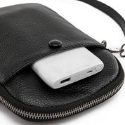 Custodia in pelle nera con power bank bianco, chiusura a zip e bottone. Accessorio elegante e pratico per ricarica dispositivi in movimento.