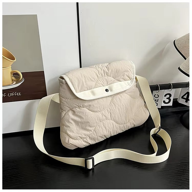 Borsa a tracolla imbottita beige su tavolo nero, design moderno, chiusura a bottone, ideale per moda casual. Accessorio versatile e trendy.