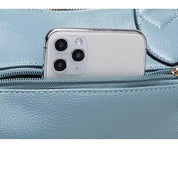 Smartphone bianco con tripla fotocamera in una tasca di borsa in pelle azzurra. Accessori moda, tecnologia, design elegante.
