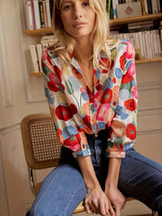 Blusa donna floreale colorata, maniche lunghe, abbinata a jeans blu. Moda casual, stile primaverile, sfondo libreria.