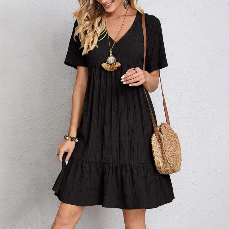 Abito estivo nero da donna con scollo a V, maniche corte e orlo a balze. Accessori: collana e borsa a tracolla in paglia. Moda casual elegante.