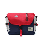 Zaino messenger multicolore con patta rossa, tasca con zip, fibbie nere e dettagli blu e grigi. Design moderno e funzionale per uso quotidiano.