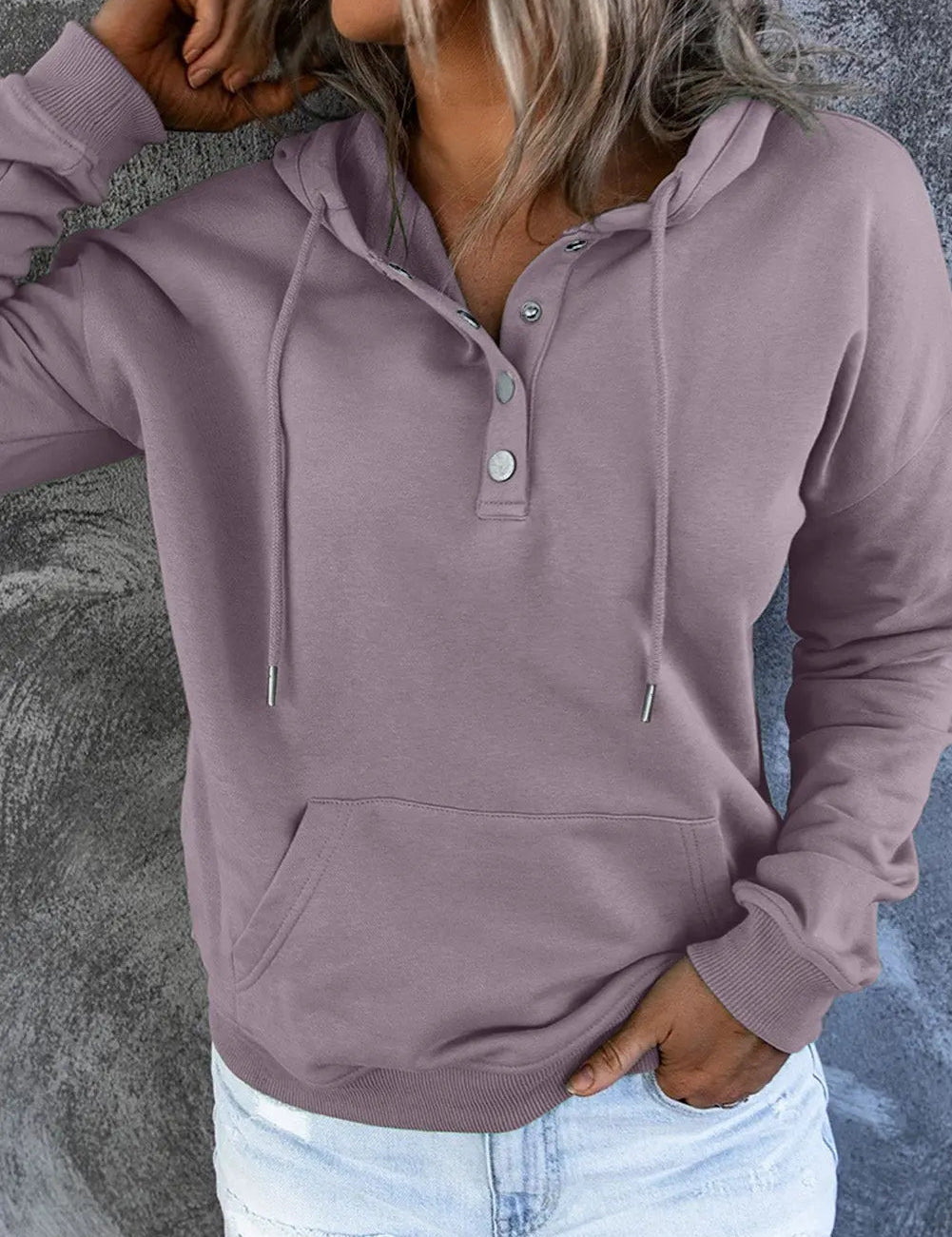 Felpa con cappuccio da donna, colore lavanda, con bottoni e tasca frontale, abbinata a jeans strappati. Look casual e moderno.