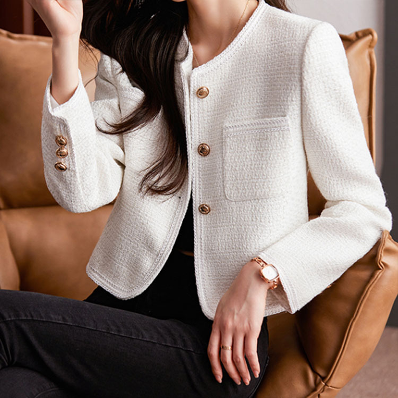 Giacca donna elegante bianca in tweed, con bottoni dorati, tasca frontale, indossata su divano marrone. Moda femminile, abbigliamento chic.