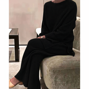 Abbigliamento donna elegante: completo maglia e pantaloni neri a coste, seduta su divano moderno. Stile casual chic, moda autunno inverno.