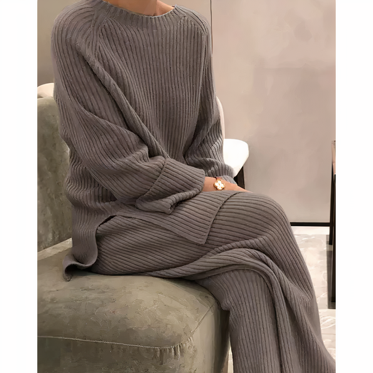 Maglione e pantaloni in maglia grigia, donna seduta su divano verde. Moda autunnale, abbigliamento casual elegante, tessuto a coste.