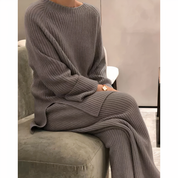 Maglione e pantaloni in maglia grigia, donna seduta su divano verde. Moda autunnale, abbigliamento casual elegante, tessuto a coste.