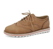 Scarpa brogue da donna in pelle marrone chiaro, suola bianca dentellata, design elegante e casual, perfetta per moda autunnale e primaverile.