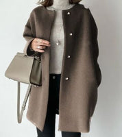 Cappotto marrone elegante con bottoni, indossato su maglione bianco. Borsa a tracolla beige, look autunnale chic. Moda donna invernale.