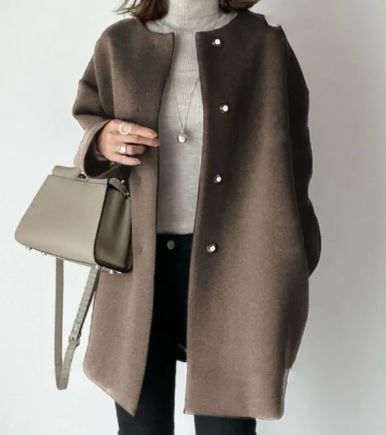 Cappotto marrone elegante con bottoni, indossato su maglione bianco. Borsa a tracolla beige, look autunnale chic. Moda donna invernale.