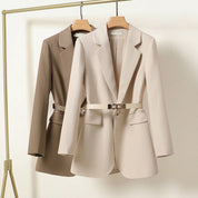 Due blazer eleganti da donna, beige e marrone, appesi su grucce. Design moderno con cintura in vita. Abbigliamento formale, moda femminile.