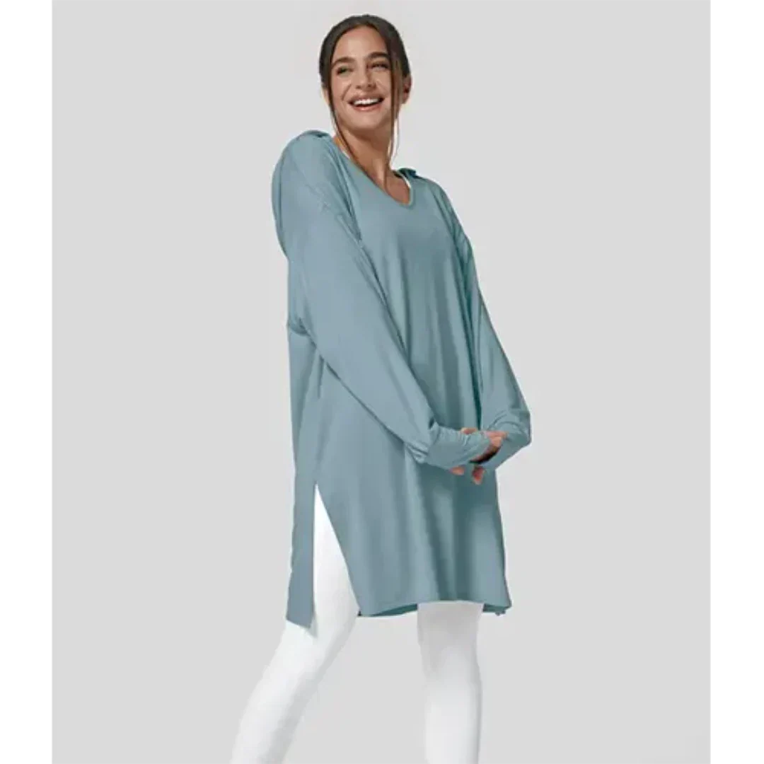 Donna sorridente indossa tunica oversize blu su leggings bianchi, moda casual donna, abbigliamento comodo, stile autunnale, sfondo grigio chiaro.