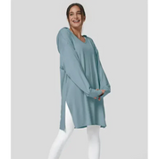 Donna sorridente indossa tunica oversize blu su leggings bianchi, moda casual donna, abbigliamento comodo, stile autunnale, sfondo grigio chiaro.