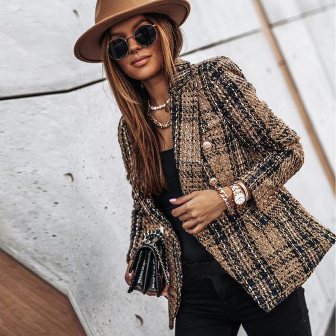 Donna alla moda con cappello marrone, occhiali da sole, giacca in tweed a quadri, collana e orologio, sfondo urbano. Stile autunnale elegante.