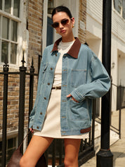 Donna con giacca di jeans oversize e abito bianco, occhiali da sole, borsa marrone, posa urbana. Moda street style autunnale.