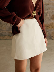 Gonna corta bianca elegante, abbinata a maglione marrone con dettaglio dorato. Moda femminile autunnale, stile casual chic.