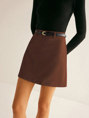 Gonna corta marrone con cintura nera, indossata con maglia nera a maniche lunghe. Elegante abbigliamento femminile autunnale.