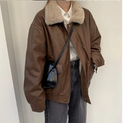 Giacca in pelle marrone con colletto in pelliccia sintetica, indossata su camicia bianca e jeans neri, borsa a tracolla nera. Moda autunnale casual.