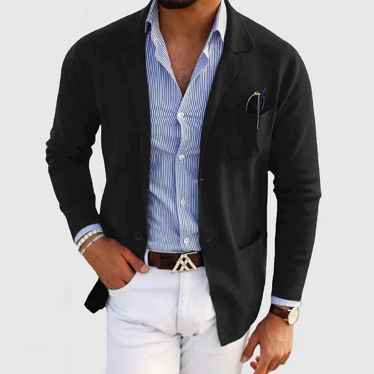 Giacca nera elegante su camicia a righe blu e pantaloni bianchi, stile casual uomo. Accessori: orologio, bracciali, occhiali da sole.