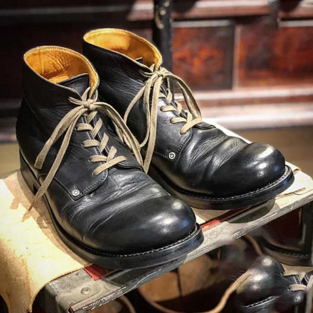 Stivali in pelle nera da uomo con lacci beige, su sfondo di legno. Scarpe eleganti e robuste, ideali per moda autunnale e invernale.